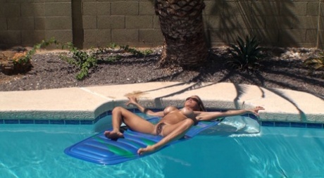 Busty Latina female lays naked atop an air mattress in swimming pool