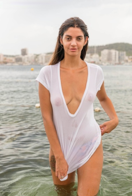 Amateur chick stands in a body of water in bikini bottoms and a wet shirt