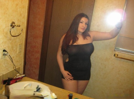 Curvy girl takes self shots in a mirror while wearing an off shoulder dress